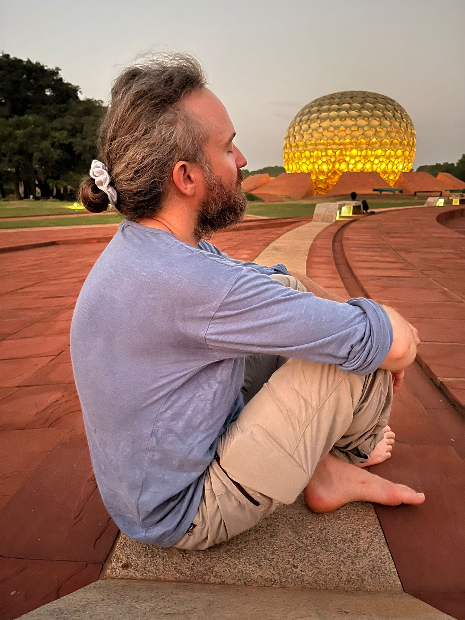 Thibaut assis en tailleur devant le Matrimandir d'Auroville, au crépuscule